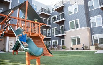 A child slides down a green slide in a playground.